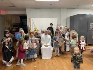 Children dressed in historical and biblical costumes standing around a priest.