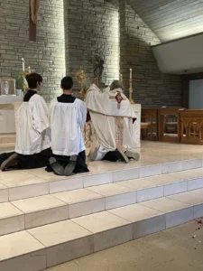 A priest and altar servers kneeling in front of the altar during adoration.